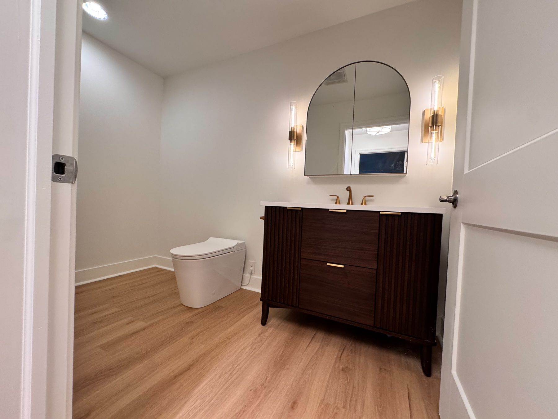 Powder room with a walnut vanity, arched mirror and brushed brass fixtures