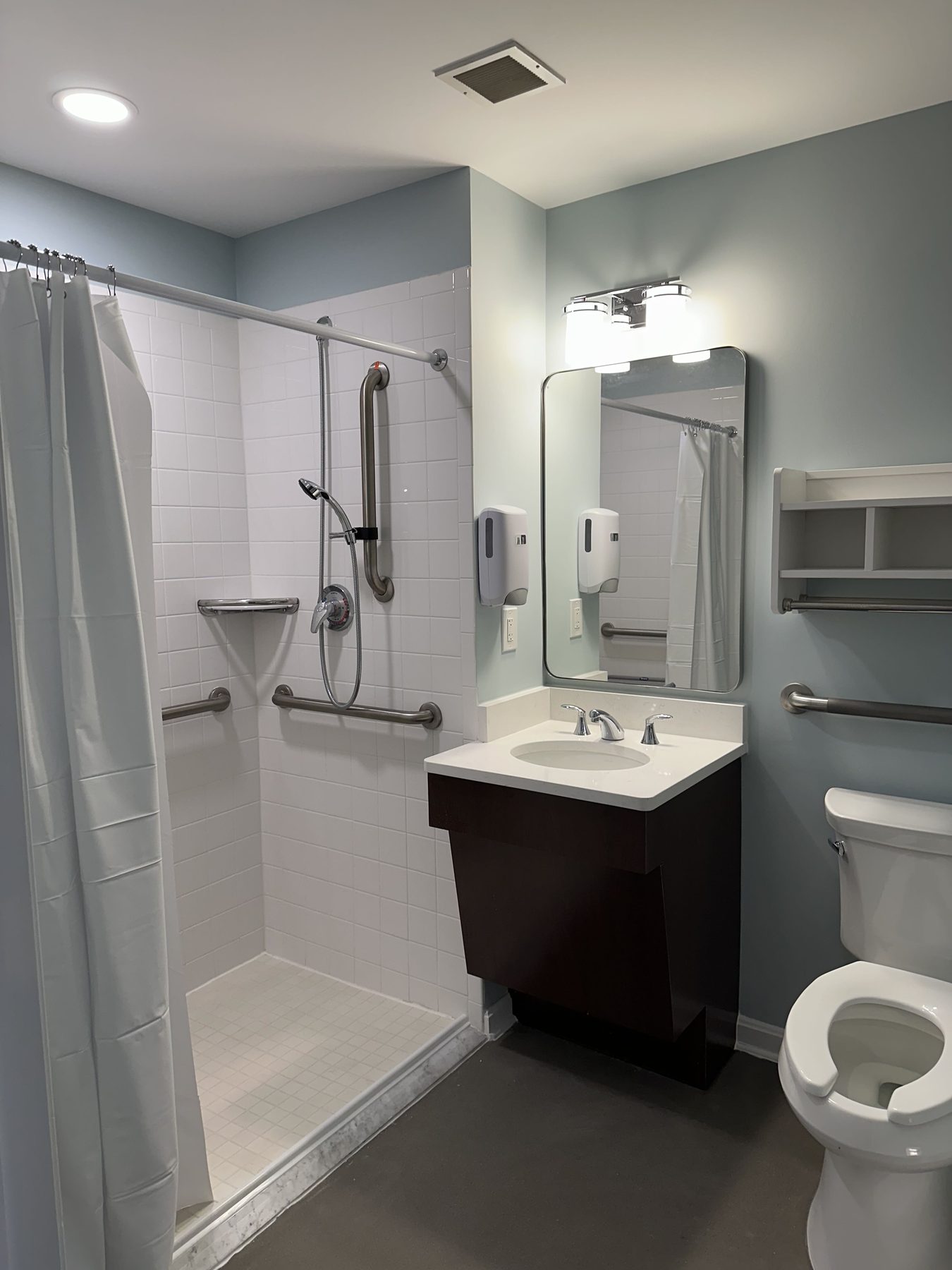 Accessible resident bathroom with a roll-in tiled shower and grab bars in an Annapolis-area healthcare facility