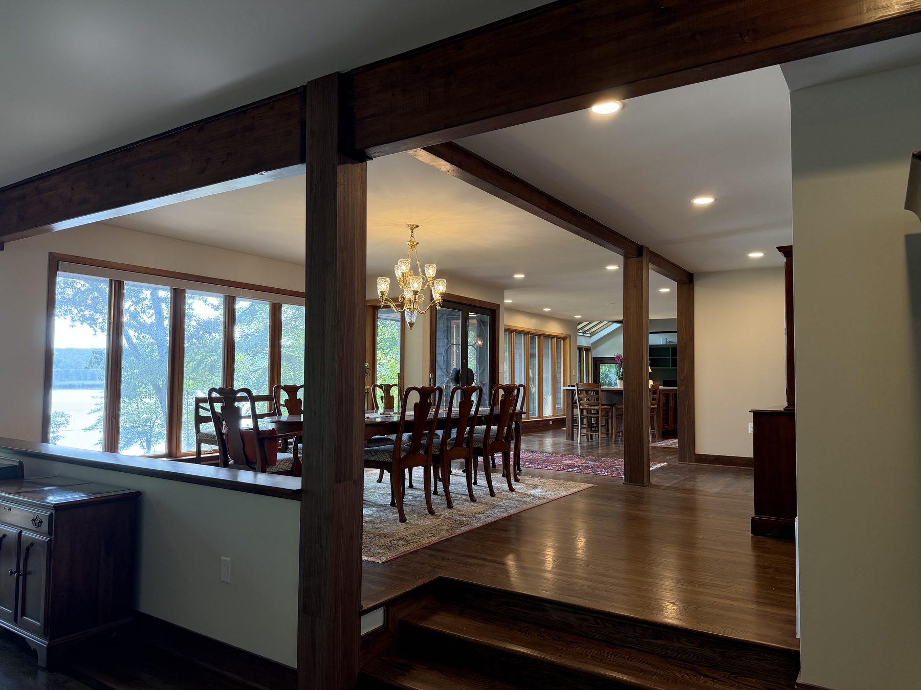 Open-plan living and dining space with structural walnut beams and a wall of windows